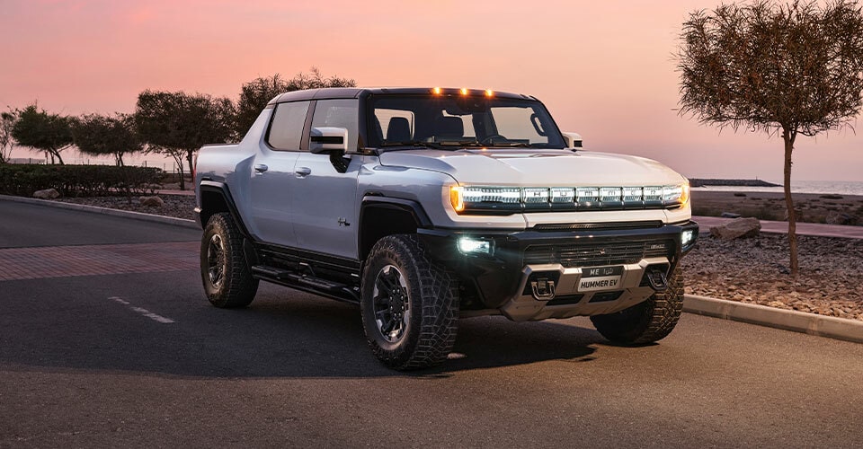 Vue latérale avant du camion GMC Hummer EV stationné sur une route avec un lac en arrière-plan.