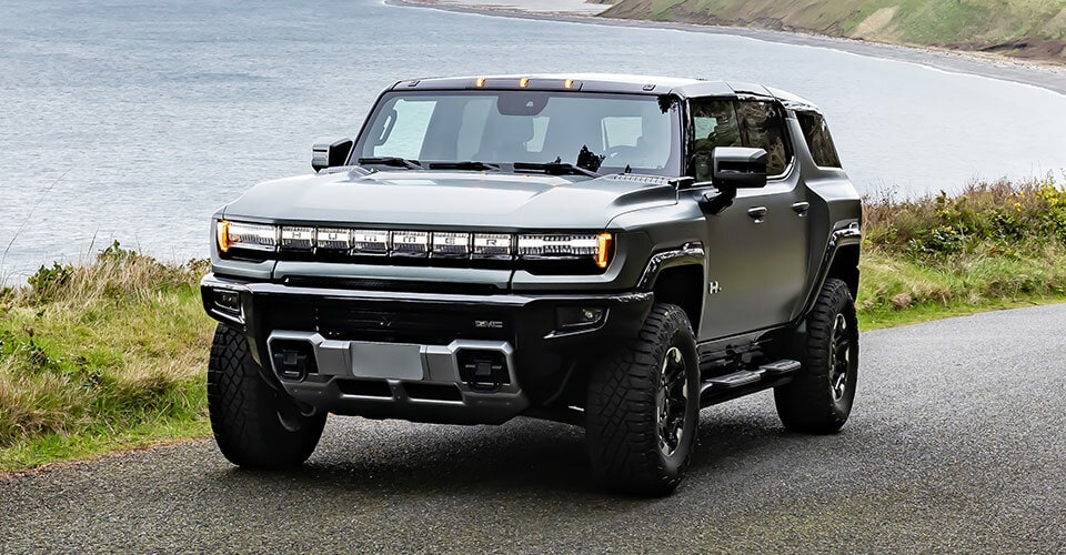 Vue latérale avant du VUS GMC Hummer EV 2024 en mouvement sur la route dans une forêt.