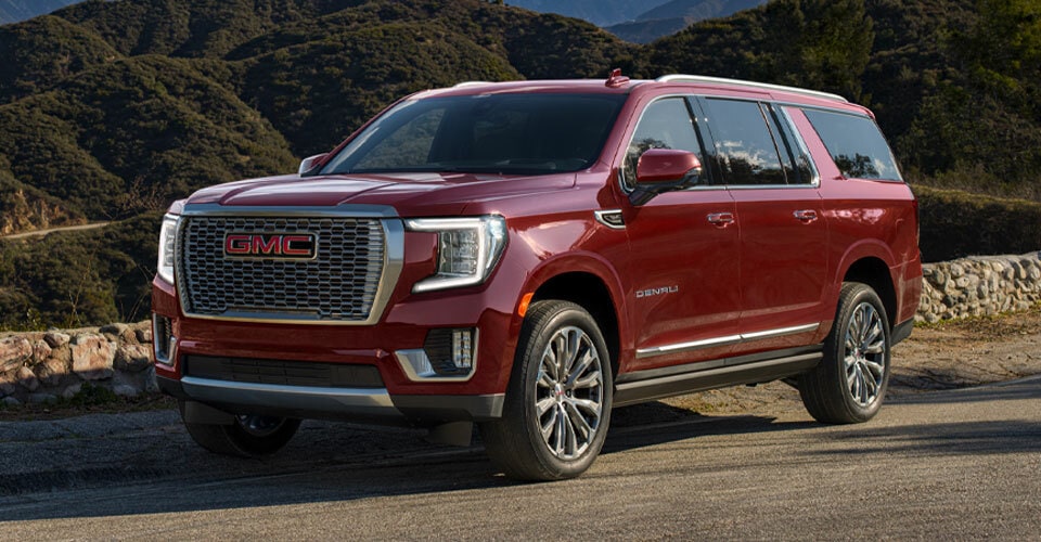 VUS pleine grandeur GMC Yukon 2024 stationné sur une route avec une colline couverte d’herbe en arrière-plan.