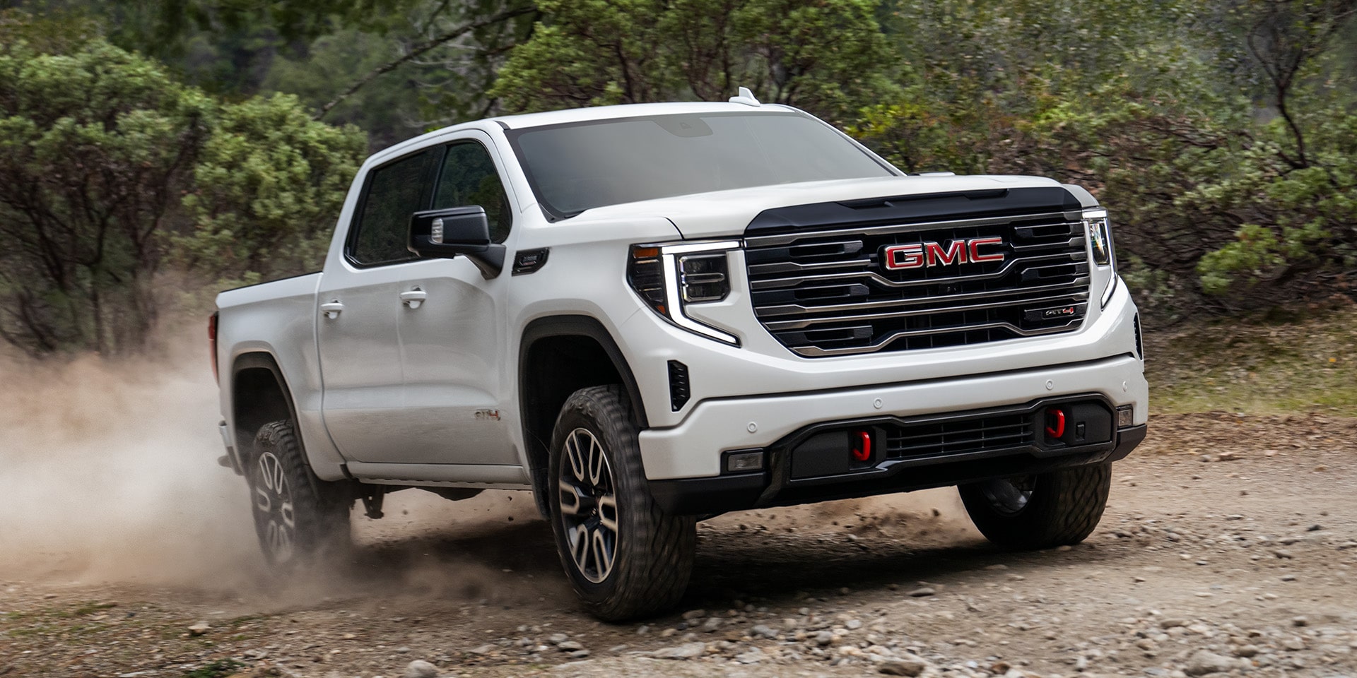 Front Three-Quarters View of the 2026 GMC Sierra AT4 1500 Pickup Truck Driving Down a Dirt Road.