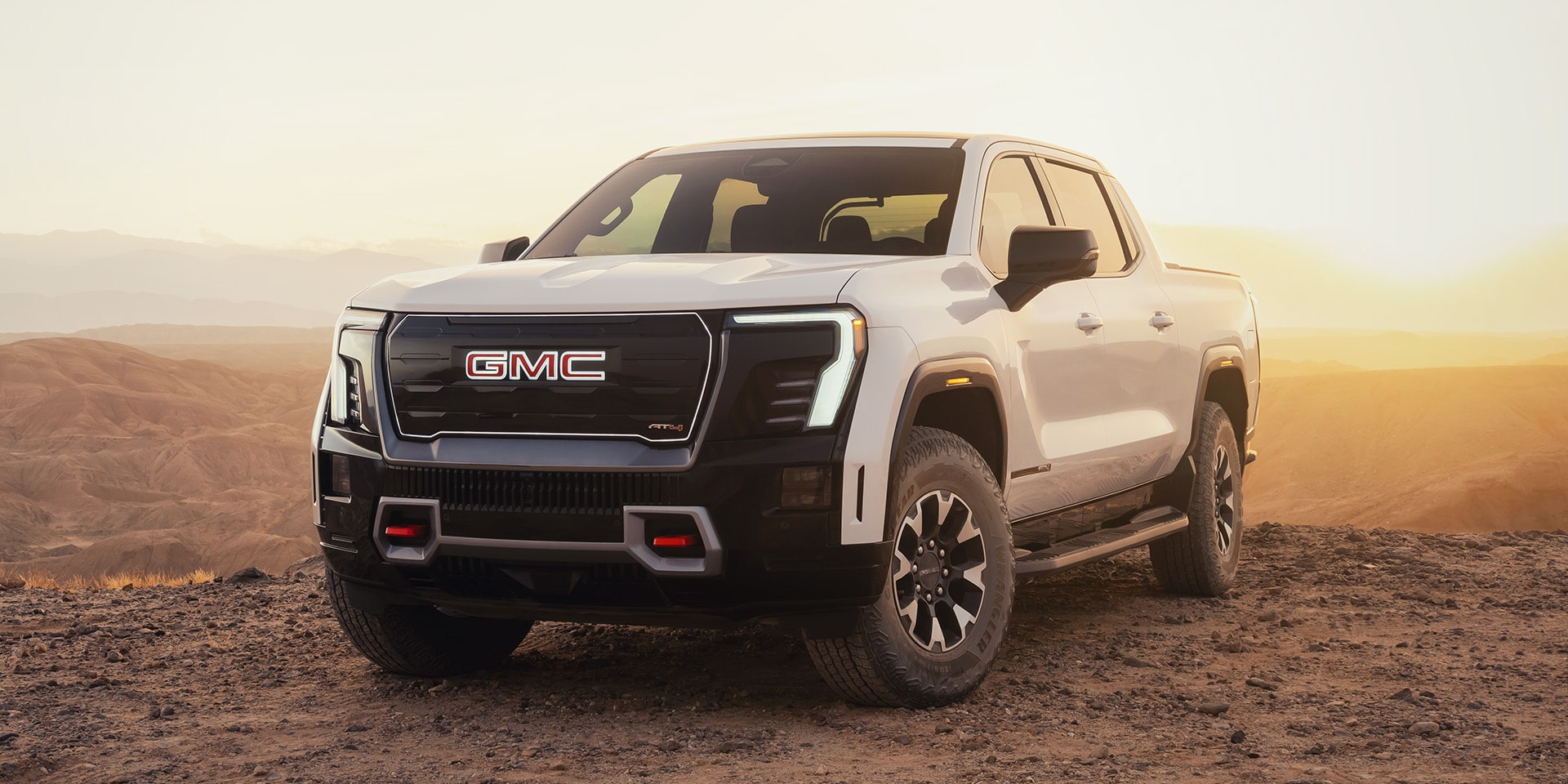 Front Three-Quarters View of the 2026 GMC Sierra AT4 EV Parked in the Desert at Sunset.