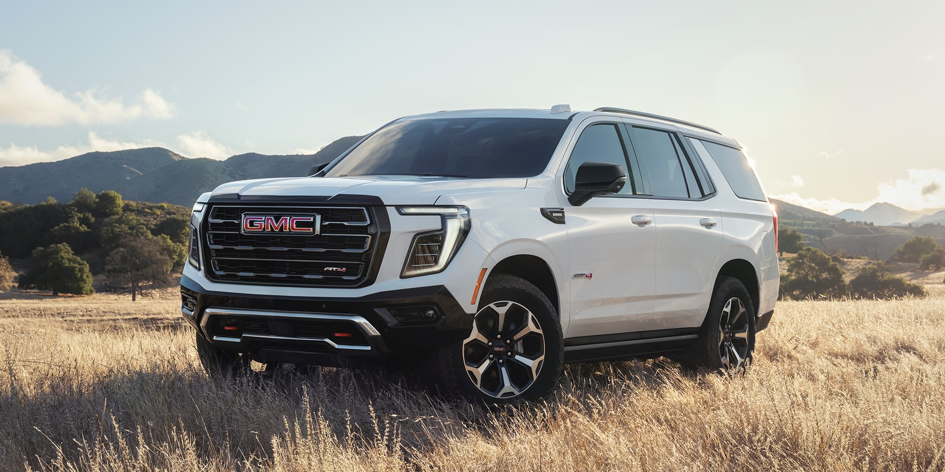 Front Three-Quarters View of the 2026 GMC Yukon AT4 Full-Size Off-Road SUV Parked on a Scenic Field.
