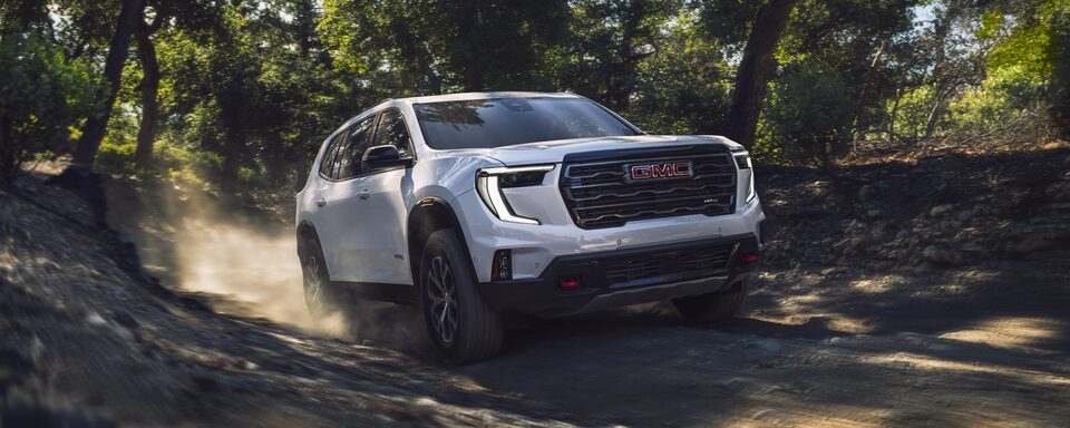 GMC Acadia AT4 2024 qui traverse un terrain accidenté dans une forêt. GMC Acadia AT4 2024 qui traverse un terrain accidenté dans une forêt.