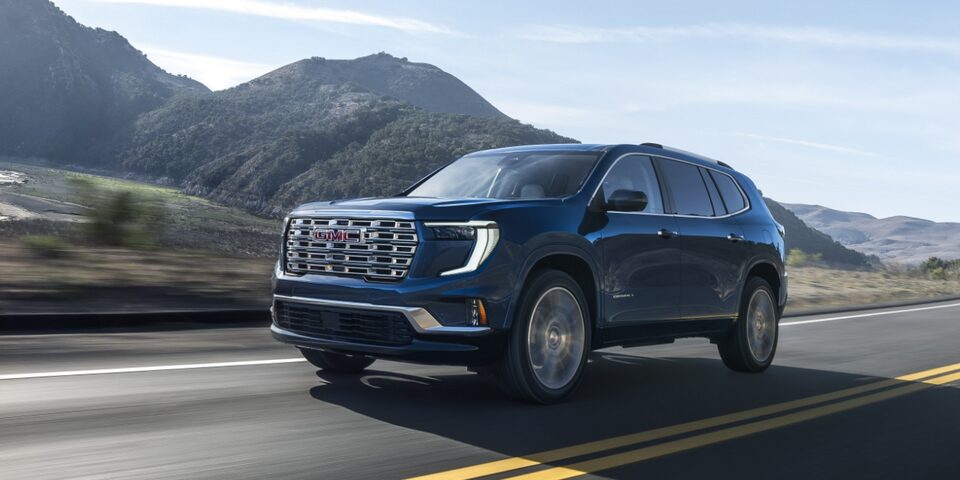 Vue latérale du GMC Acadia Denali 2024 en mouvement seul sur une route à flanc de montagne.