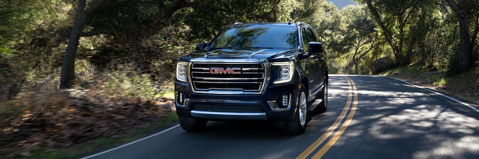 2024 GMC Yukon SLE and SLT driving alone on a forest road.