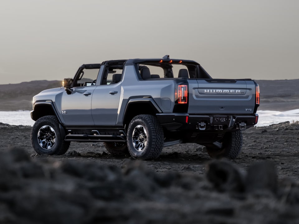 Vue latérale arrière du camion GMC Hummer EV 2025 stationné sur un chemin rocailleux avec les panneaux de toit retirés.