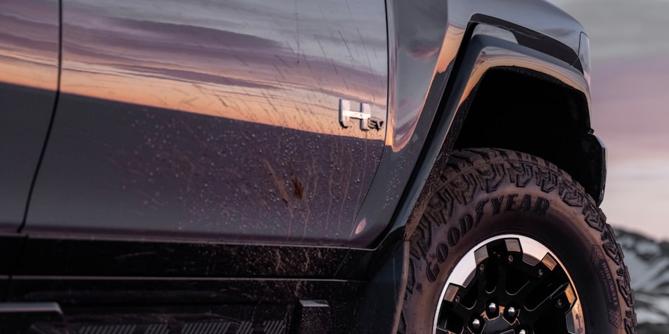 Low angle side view of the front tire of the 2025 GMC Hummer EV SUV under an evening sky.