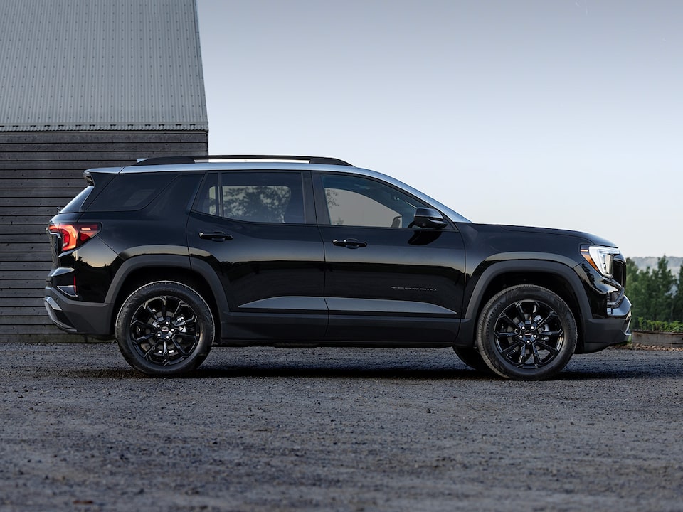 Side view of the 2025 Terrain parked near a wooden house.