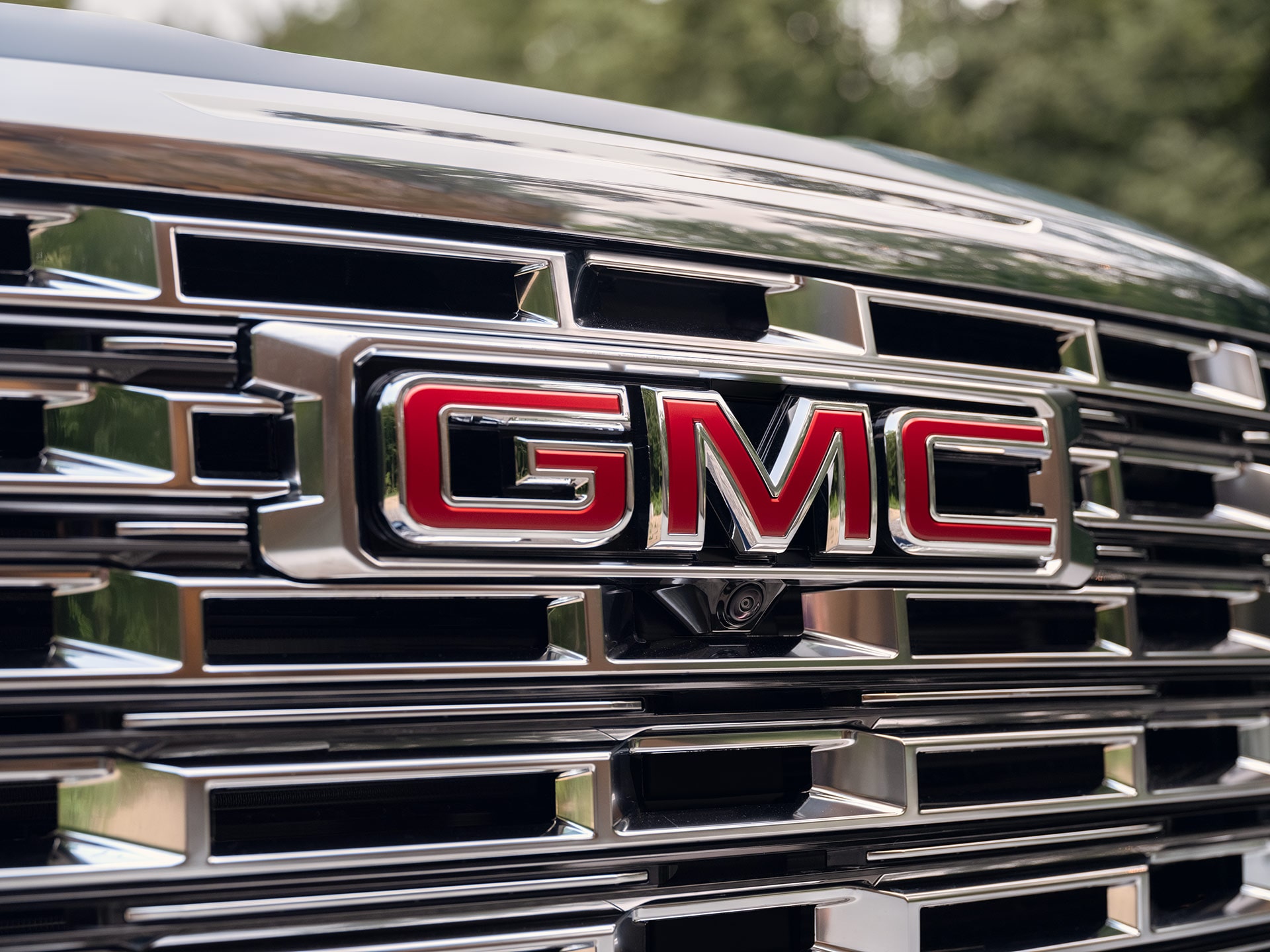 Un gros plan sur la calandre avant d’un VUS GMC Acadia 2027 avec un logo GMC rouge au centre.