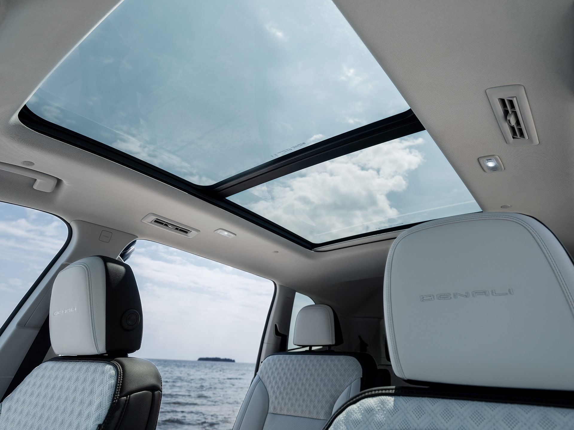 Un toit ouvrant panoramique dans un VUS GMC Acadia 2027 depuis les sièges arrière avec vue sur l’océan.