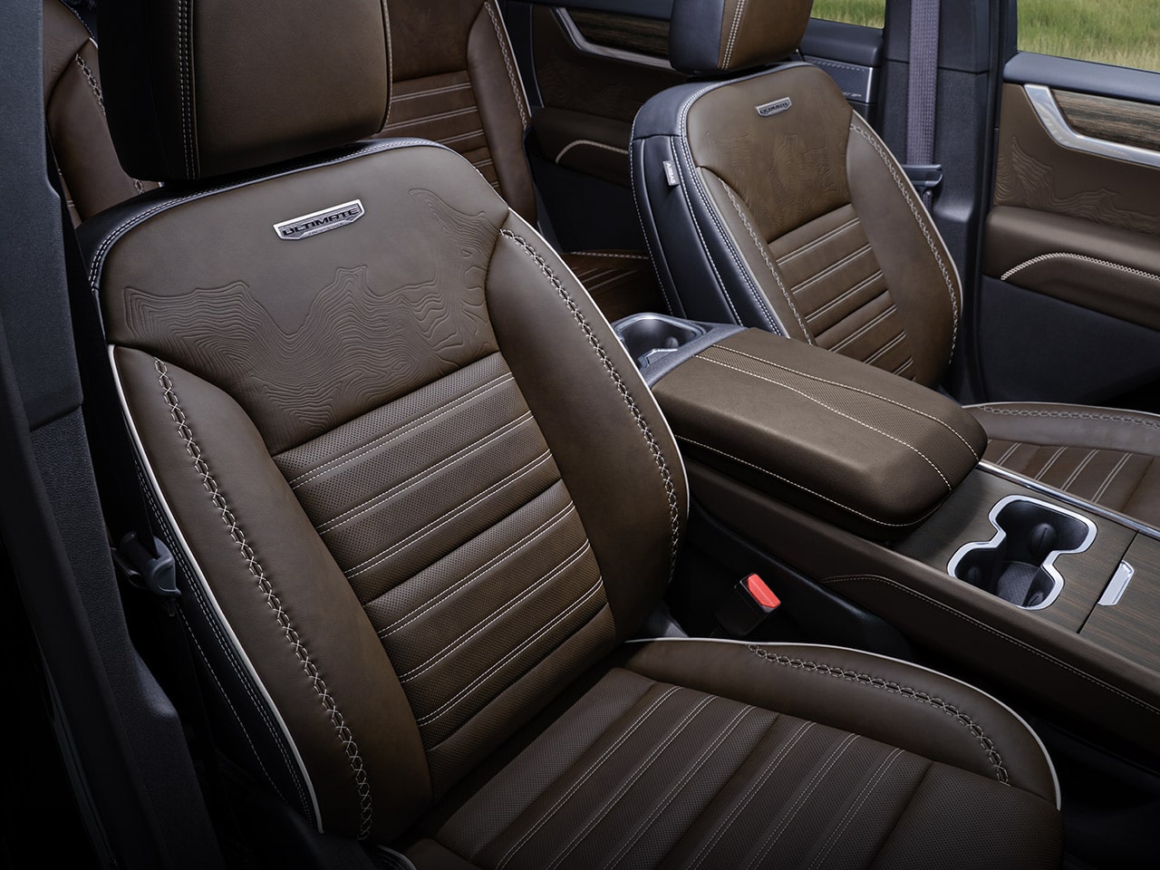 Un gros plan des sièges en cuir brun avec des coutures blanches et l’emblème ultime dans l’intérieur d’un VUS GMC Acadia 2027.