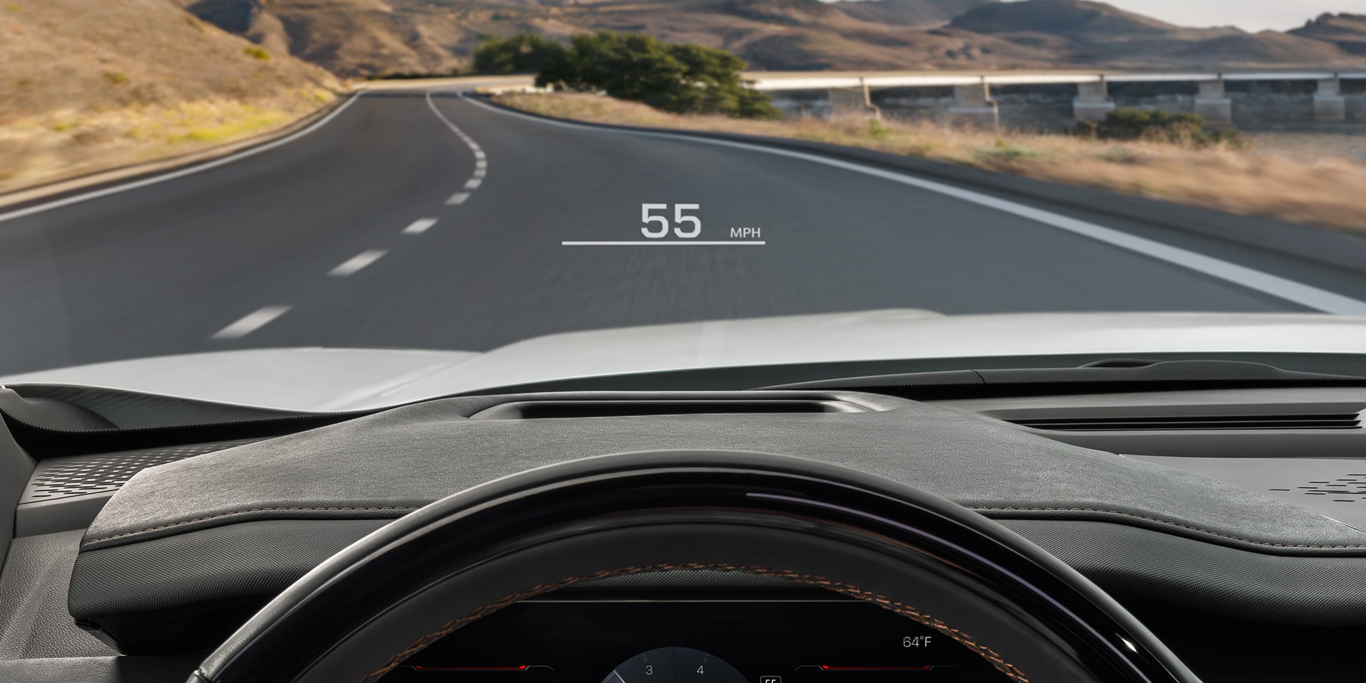 La perspective du conducteur à l’intérieur d’un VUS GMC Acadia 2027, mains sur le volant, montrant le tableau de bord numérique et la route devant vous.