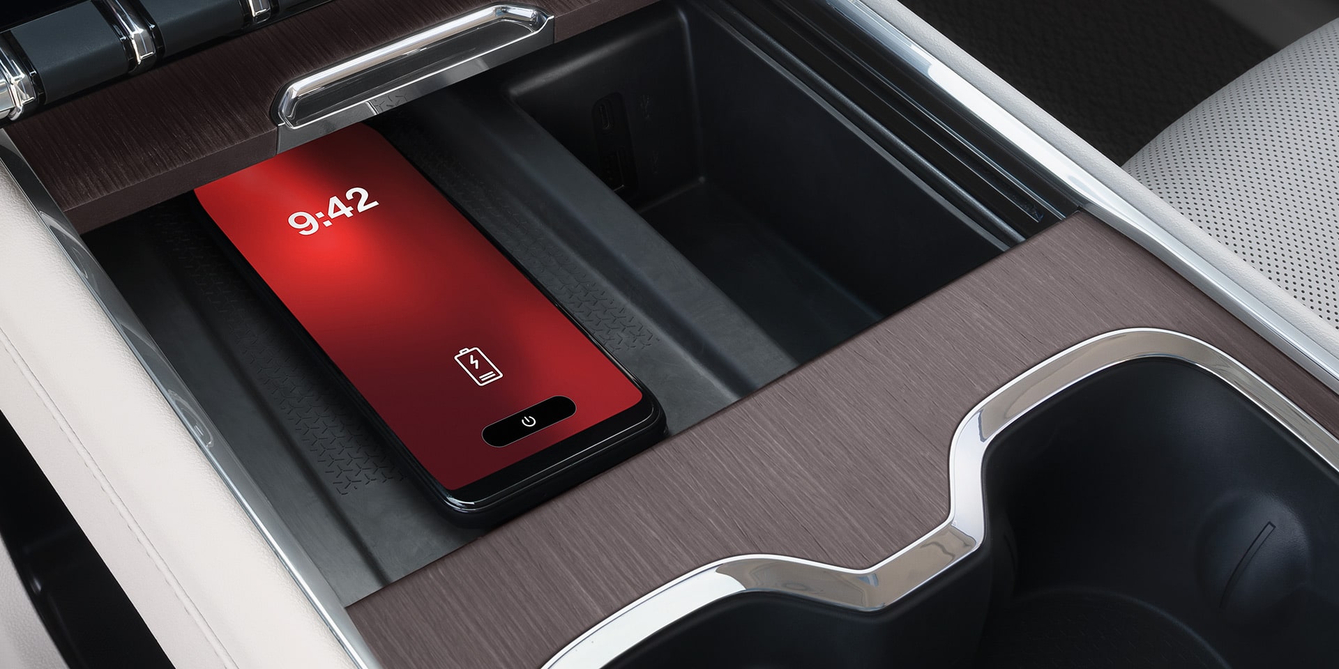 Un téléphone intelligent rouge se recharge sans fil dans un compartiment central de la console intérieure d’un VUS GMC Acadia 2027.