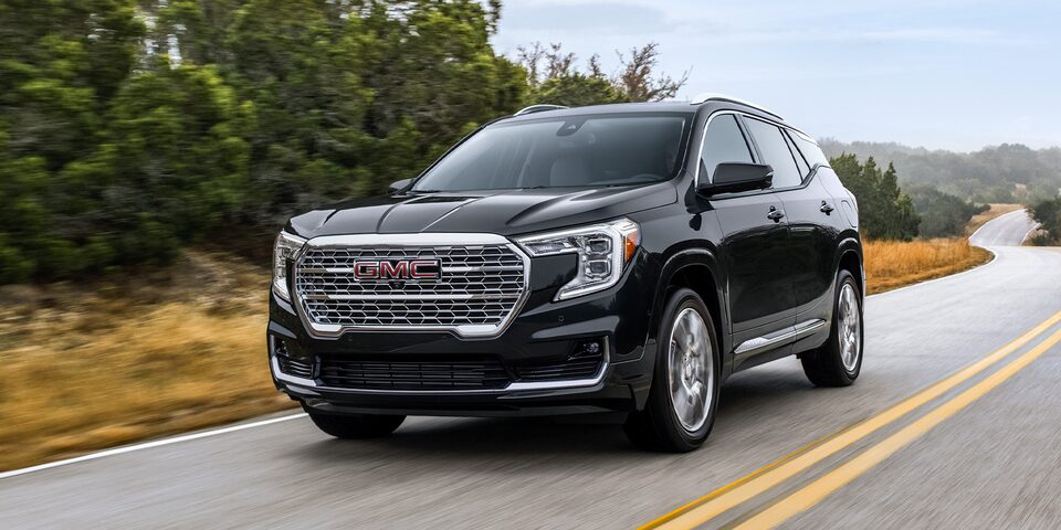 The 2024 GMC Terrain Denali driving on the road highlighting its chrome accents.
