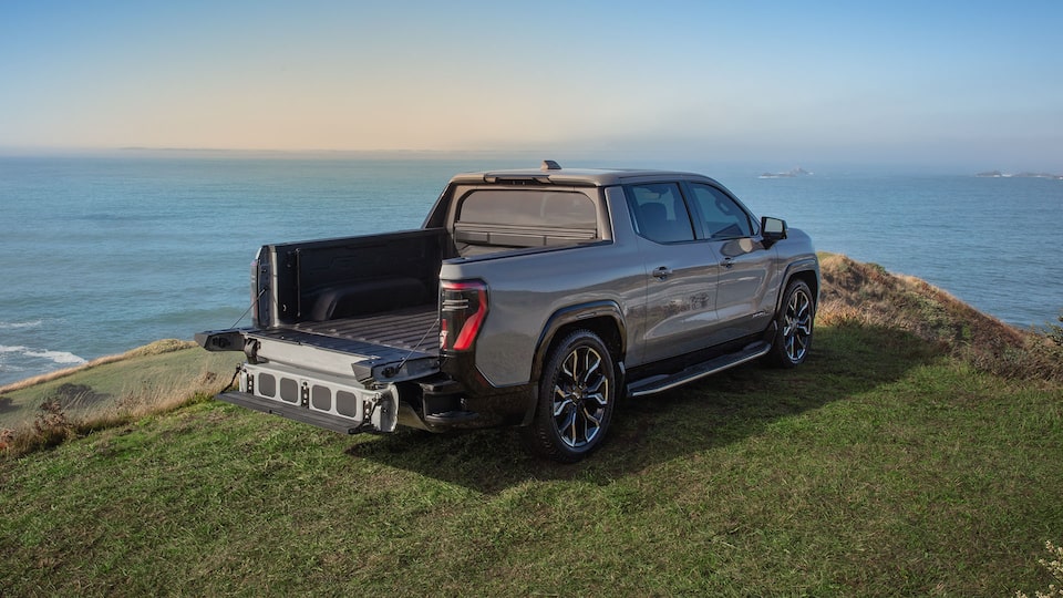 Back-side view of the 2025 GMC Sierra EV Denali parked on a cliff with its trunk bed lowered.