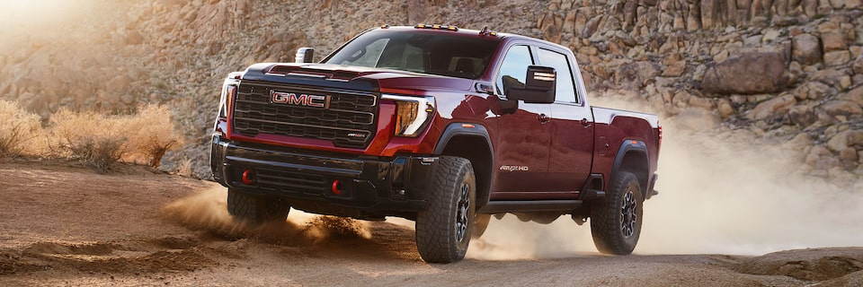 Vue latérale avant du camion GMC Sierra HD AT4 2025 en mouvement dans les montagnes.