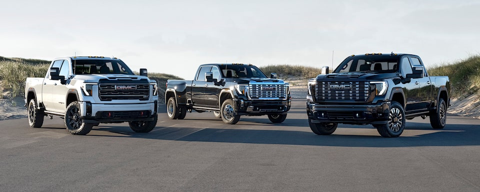 Trois camions GMC Sierra HD 2025 stationnés les uns à côté des autres à l’extérieur par une journée ensoleillée.