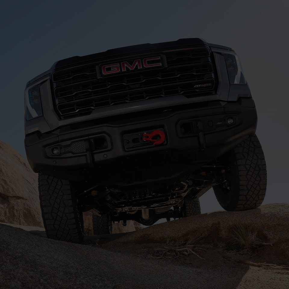 Vue rapprochée de la calandre et du dessous d’un camion GMC Sierra HD 2025 stationné sur un terrain accidenté.