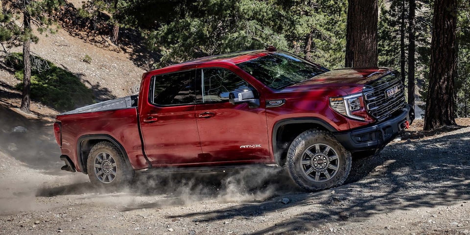 Un pick-up GMC Sierra 1500 rouge en conduite hors route dans la forêt.
