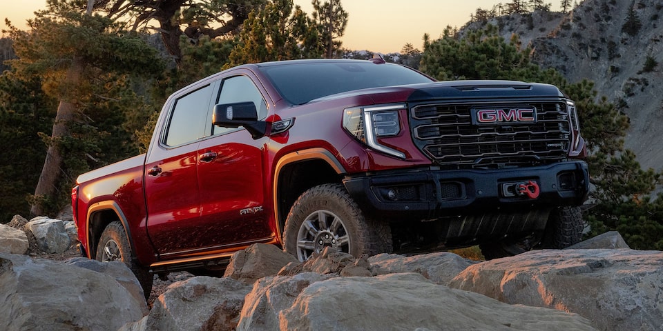Un pick-up GMC Sierra 1500 rouge en conduite hors route sur un terrain rocailleux.