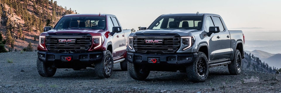 Vue avant des GMC Sierra AT4 et AT4X à côté l’un de l’autre avec des montagnes en arrière-plan.