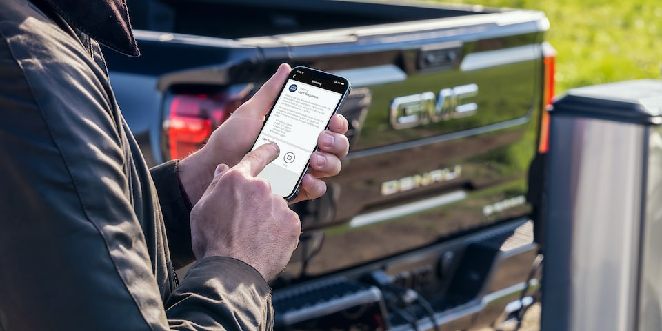 A person using the myGMC Mobile App on his phone outside a GMC vehicle.