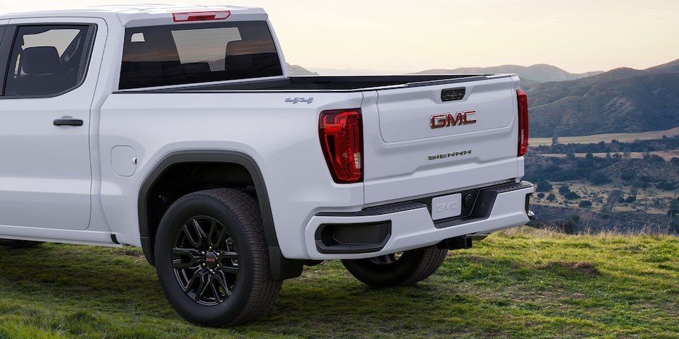 Side-back view of the 2024 GMC Sierra 1500 SLE parked on a grassy terrain by the hillside.