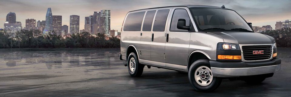 Fourgonnette de tourisme GMC Savana 2023 devant un paysage urbain.