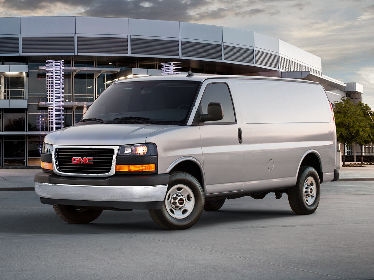 Front Three-Quarter View of a 2026 GMC Savana Cargo Van Parked outside a Modern Building.