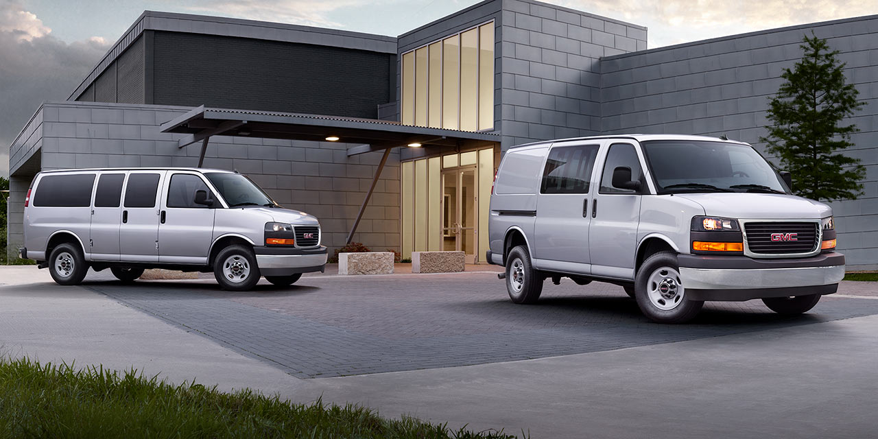Two 2026 GMC Savana Vans, a Passenger and a Cargo Van, Parked outside a Modern Building.