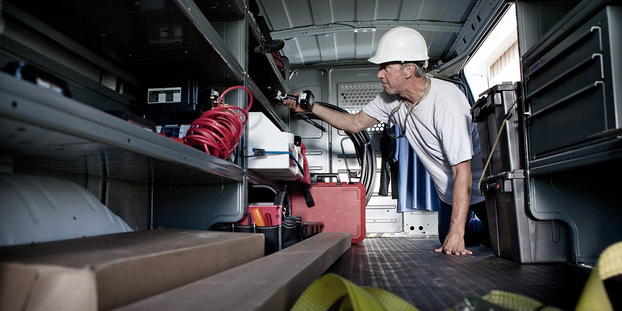 Interior View of a 2026 GMC Savana Cargo Van as a Worker in a Hard Hat Reaches for Tools.