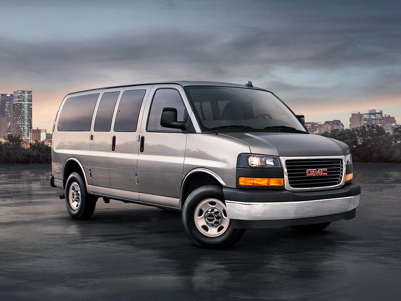 Vue latérale avant de la fourgonnette de tourisme GMC Savana 2026 avec une ville en arrière-plan.