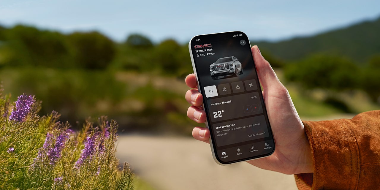 Une personne tient dans sa main un téléphone intelligent sur lequel on voit des renseignements sur le véhicule sur l’appli myGMC.