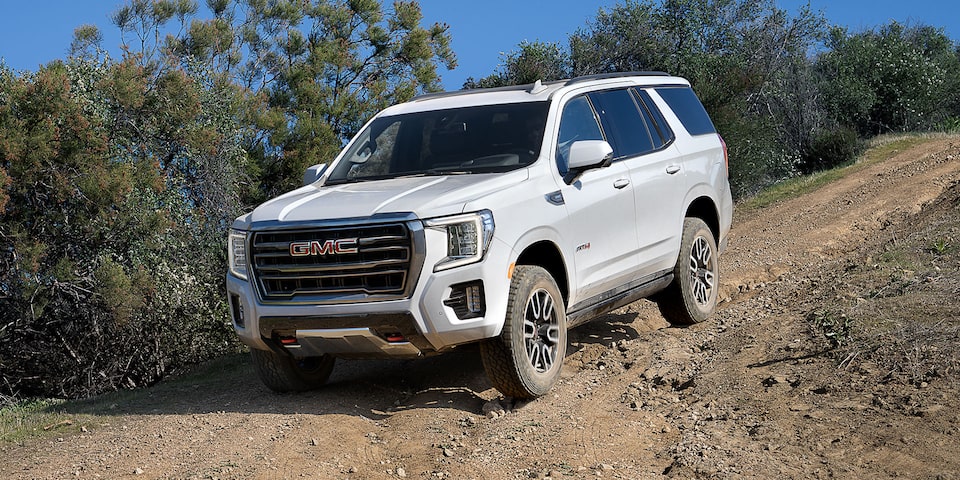 2024 GMC Yukon AT4 driving downhill on a dusty road.