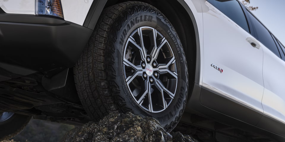 Close up view of the wheel of the 2025 GMC Acadia AT4 perched atop a rock.