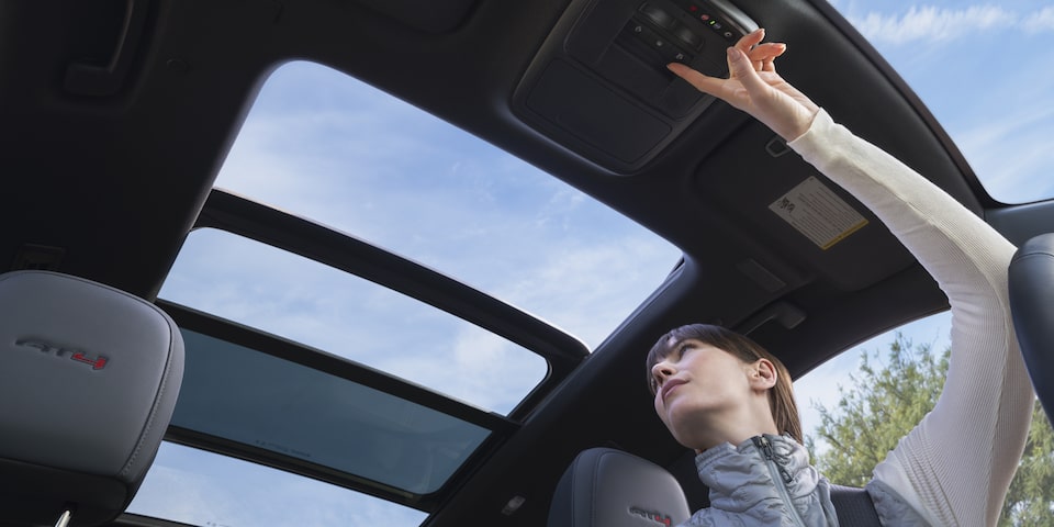 A person opening a button for the sunroof of the 2025 GMC Acadia AT4.