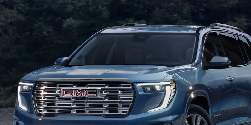 Front view of the 2025 GMC Acadia Denali parked outside a forest lodge.