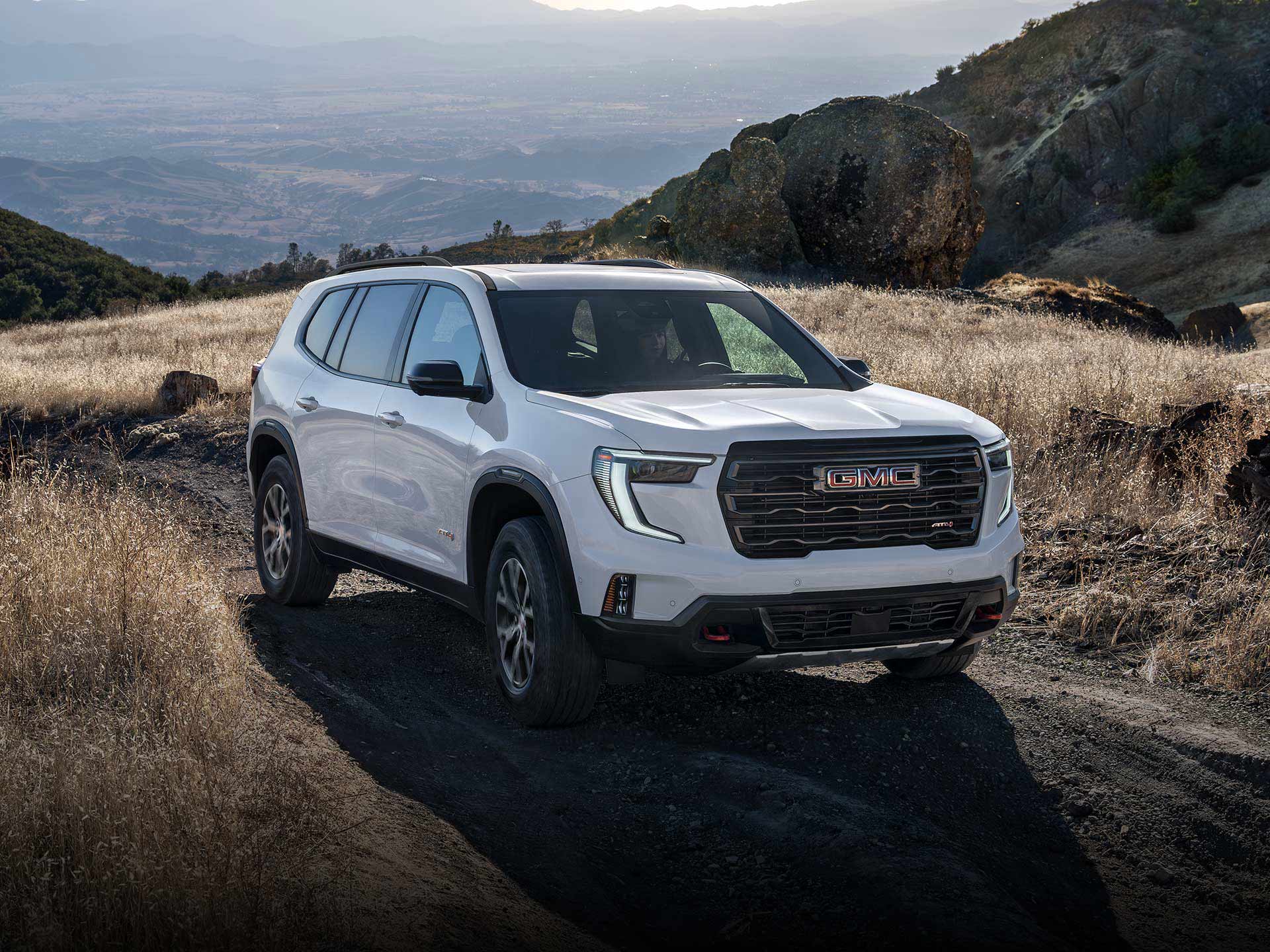 VUS intermédiaire GMC Acadia AT4 2026 roulant hors route avec des montagnes au loin.