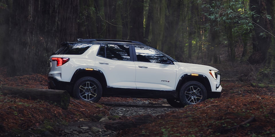 Vue latérale du VUS compact hors route GMC Terrain AT4 2026 en mouvement dans la forêt.