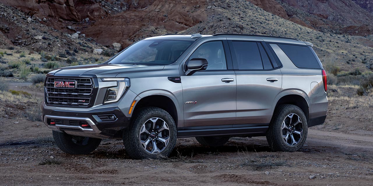 Vue latérale avant du VUS tout-terrain pleine grandeur GMC Yukon AT4 2026 stationné devant une superbe chaîne de montagnes.