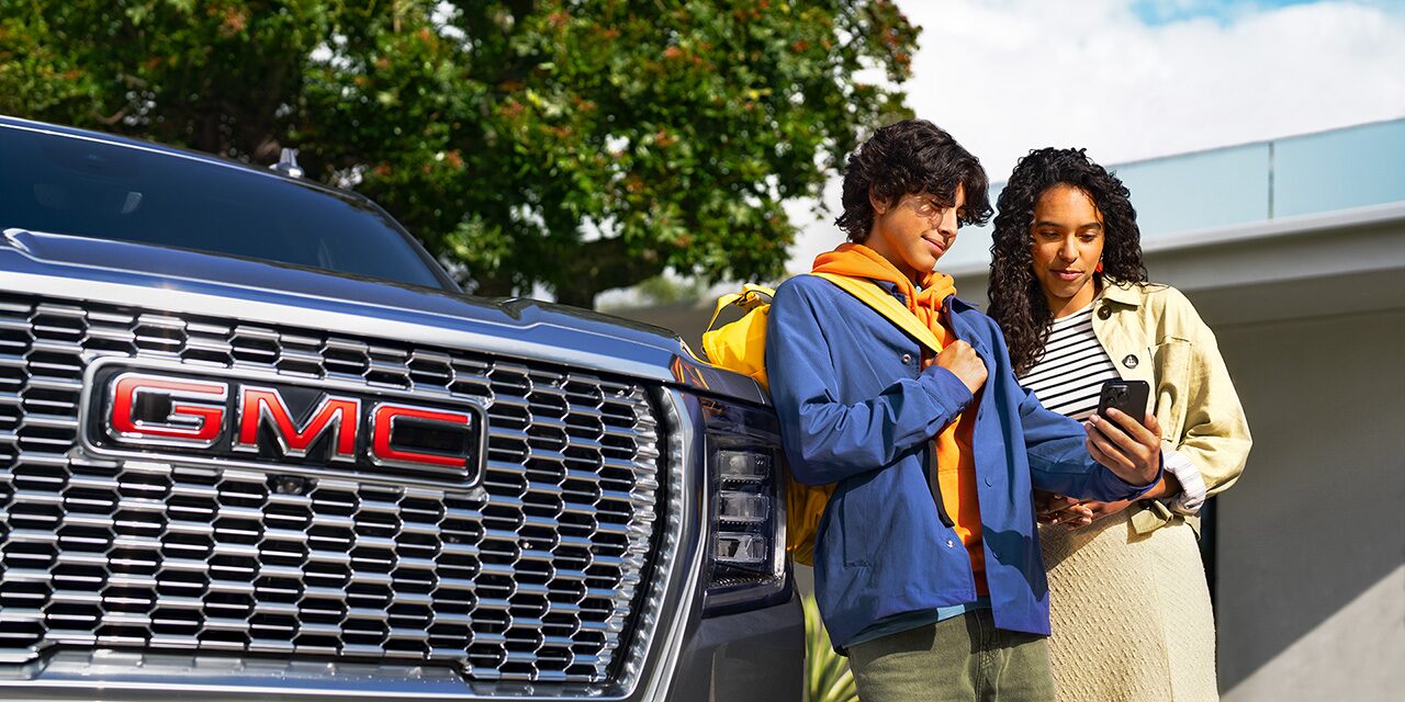 Deux personnes se tiennent debout devant un GMC Yukon 2026 en utilisant des téléphones intelligents.