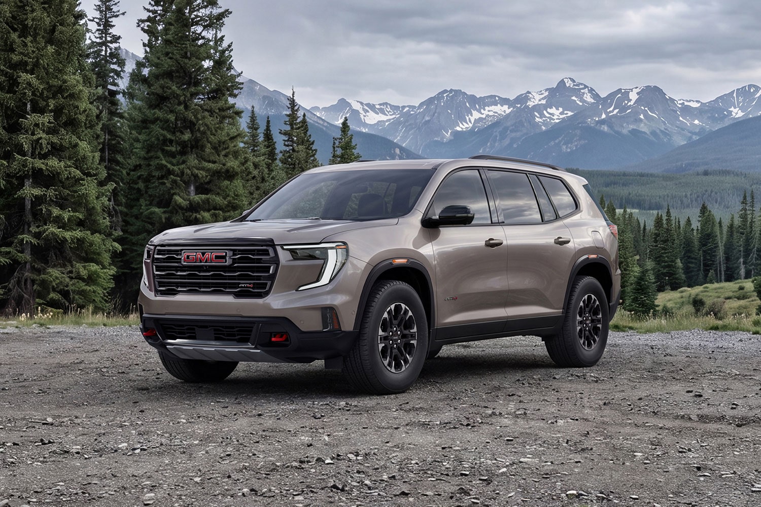 Un VUS GMC Acadia AT4 2027 stationné sur un chemin de terre devant des pins et des montagnes enneigées.