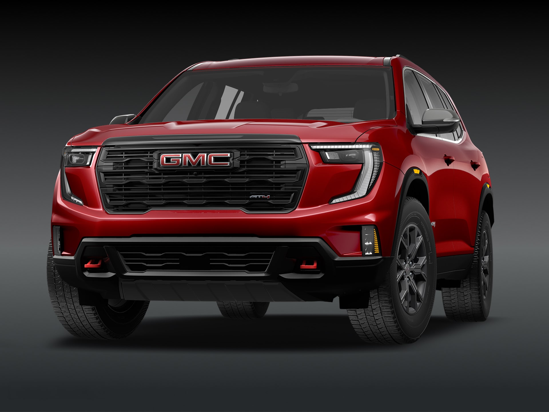Vue de trois quarts avant du SUV GMC Acadia AT4 2027 de couleur « Volcanic Red Tintcoat » sur fond sombre.