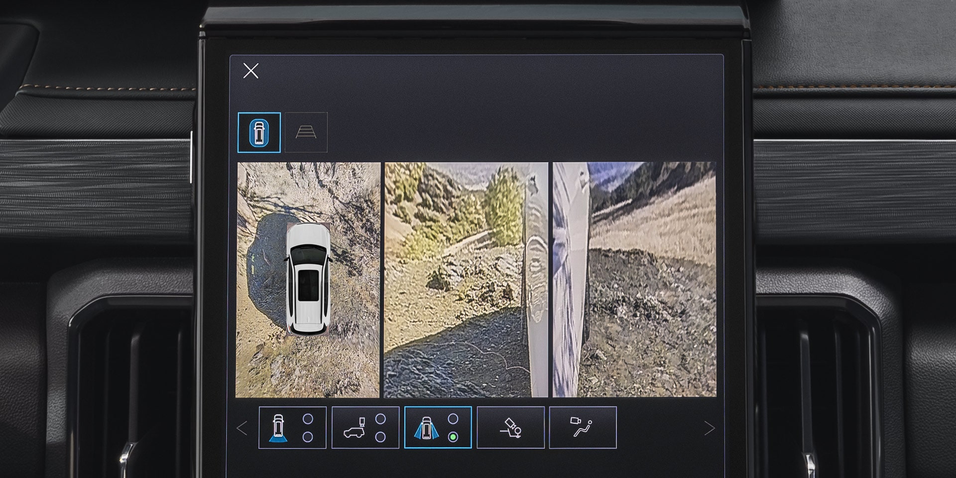 Un gros plan de l’écran d’infodivertissement d’un VUS GMC Acadia 2027 montrant une vue divisée d’un VUS blanc vue d’en haut et une vue latérale d’un chemin rocheux et inégal.