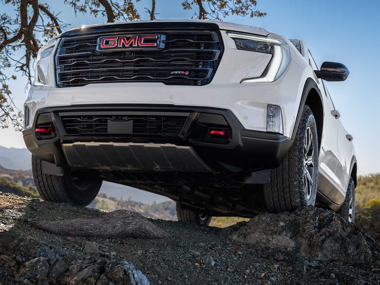 Vue de face d’un VUS GMC Acadia blanc 2027 avec le logo GMC sur la calandre, stationné sur des rochers irréguliers.