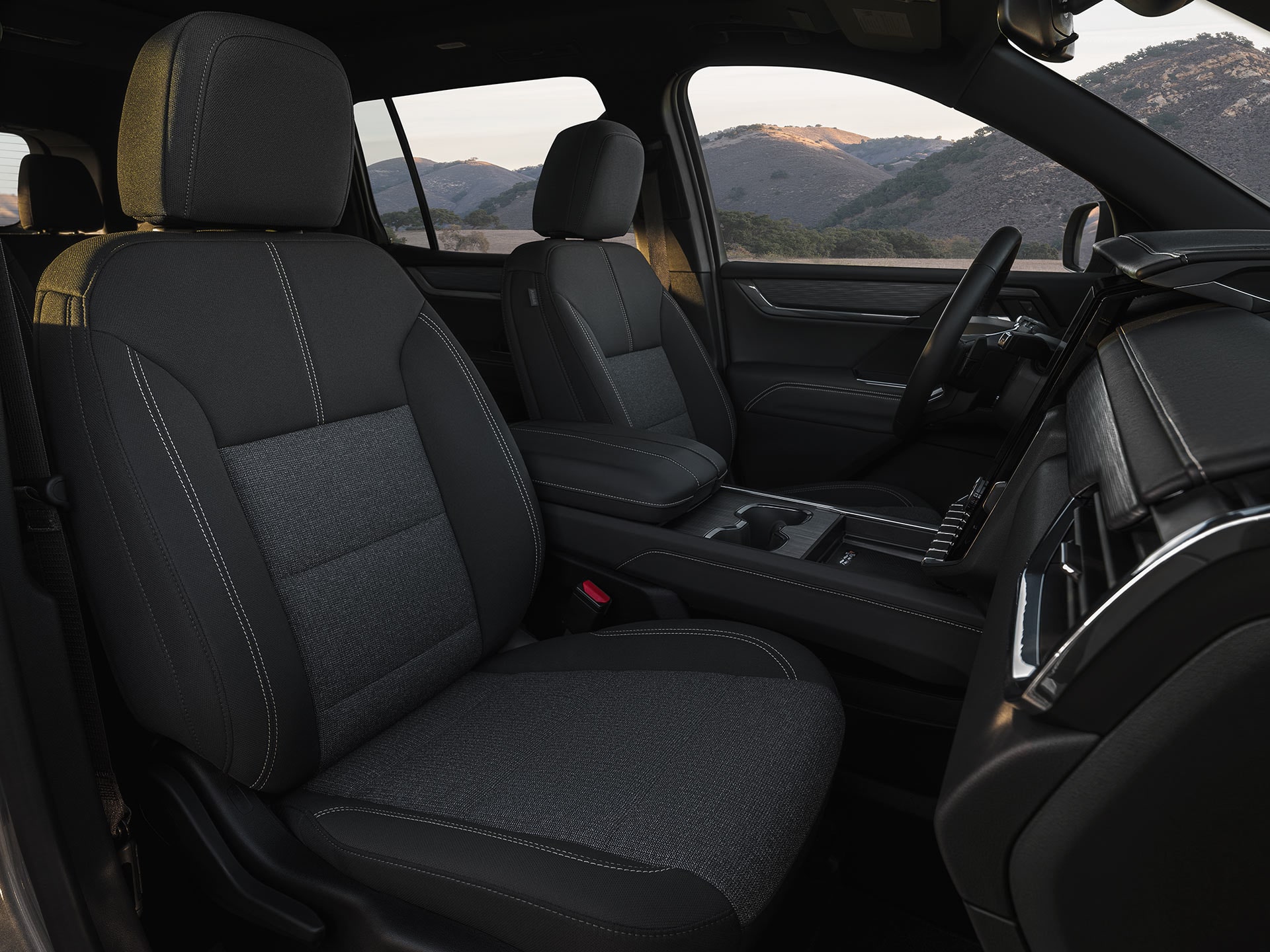 Une vue intérieure d’un VUS GMC Acadia 2027 avec des sièges avant en tissu gris et un décor montagneux pittoresque.