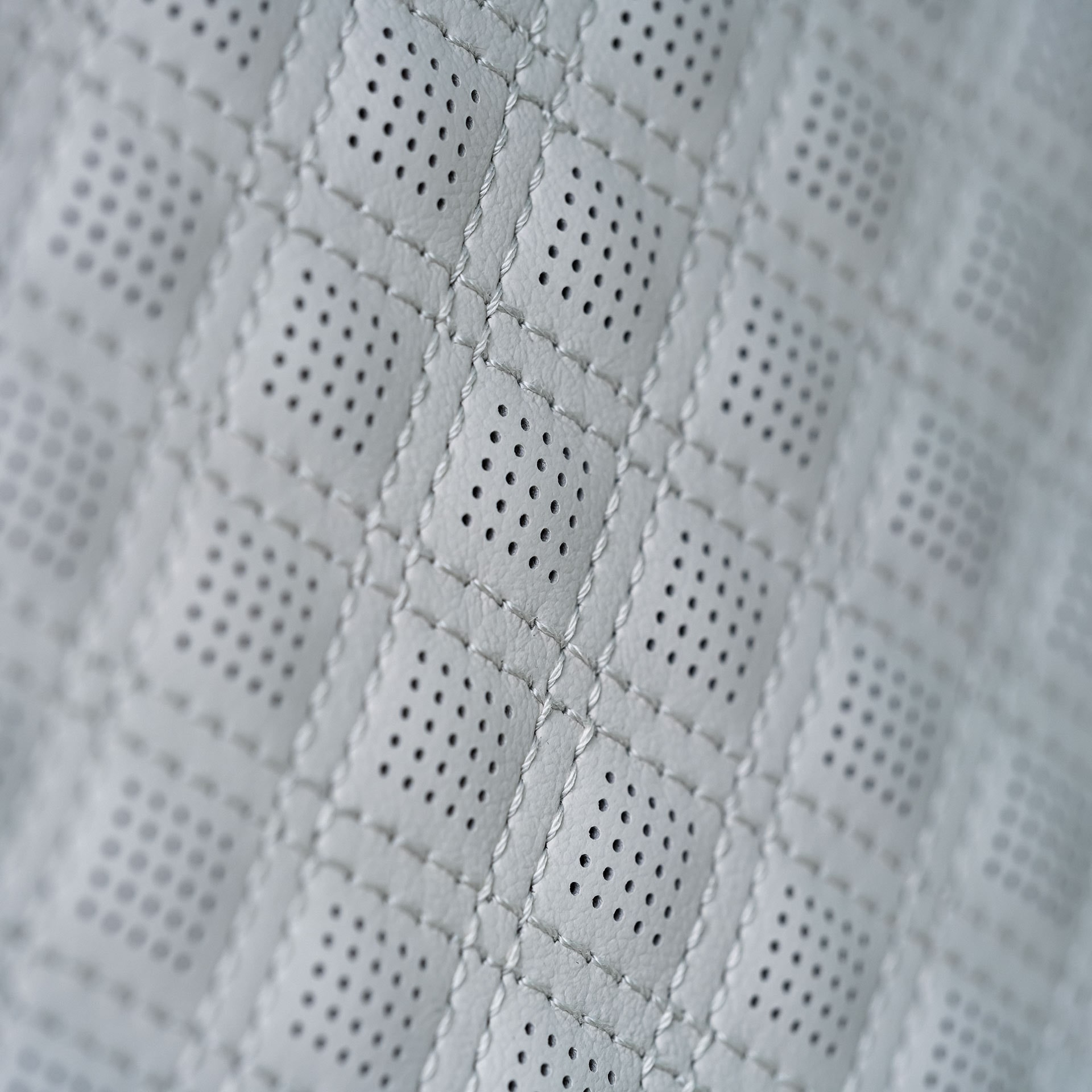 Vue rapprochée d’un siège en cuir perforé quilté gris clair avec des coutures en losange.
