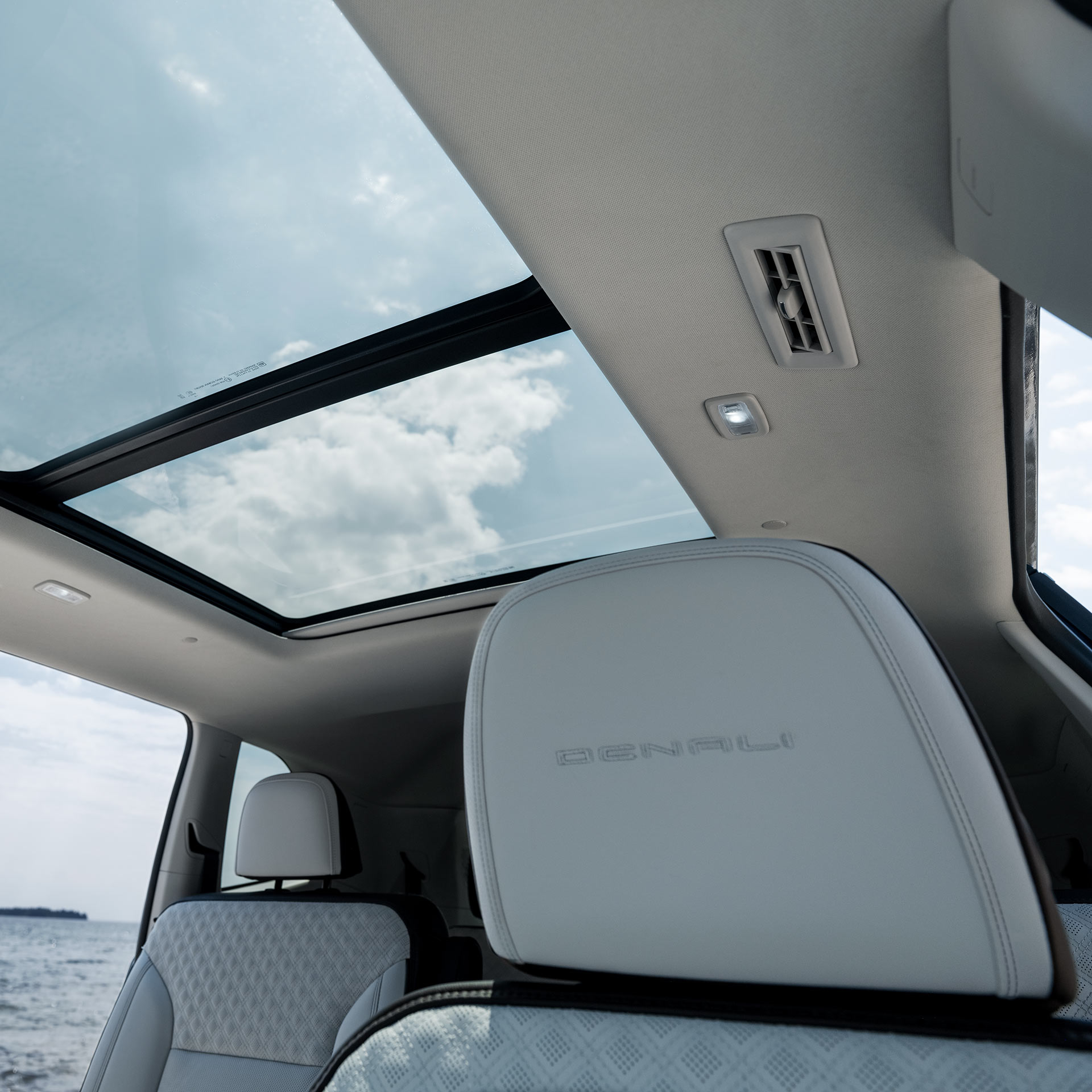 Un toit ouvrant panoramique dans un VUS GMC Acadia 2027 depuis les sièges arrière avec vue sur l’océan.