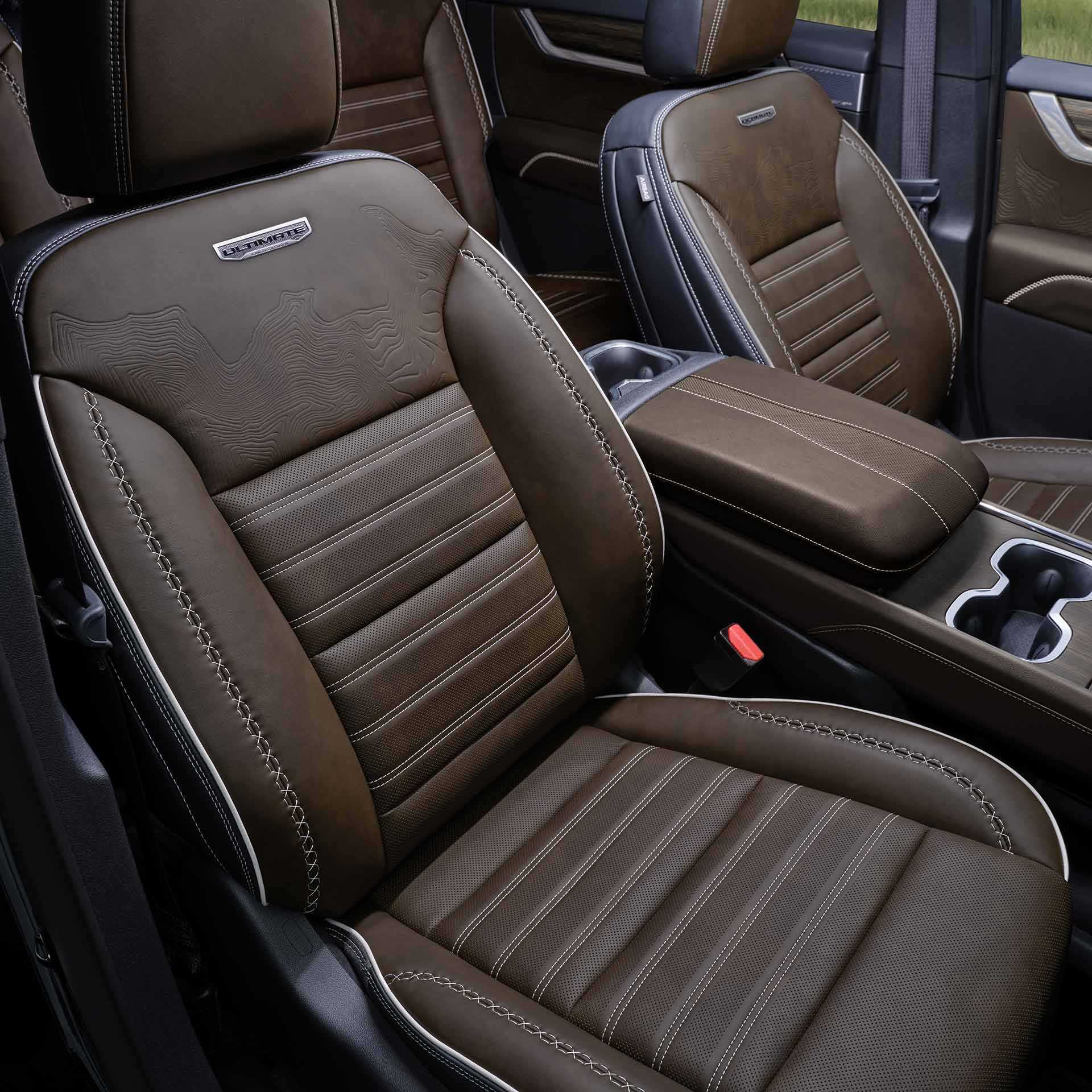 L’intérieur d’une GMC Acadia Denali 2027 avec des sièges en cuir brun ornés de coutures blanches et le logo Denali.