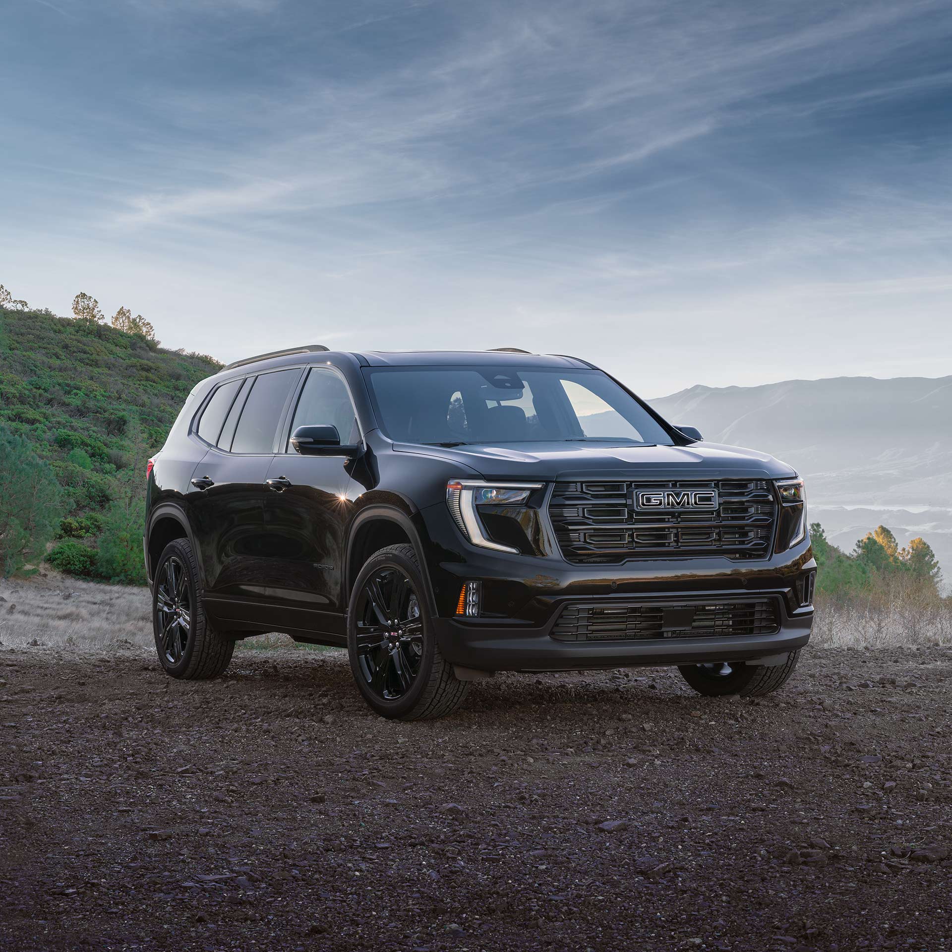 Un VUS GMC Acadia noir 2027 stationné sur une route de terre avec une calandre arborant un logo GMC argenté.